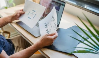 Persona sentado en escritorio frente a computadora analiza dos imágenes impresas.